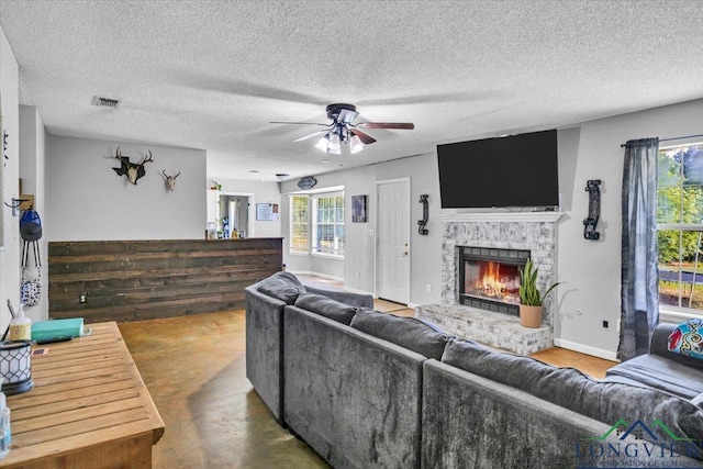 living room with ceiling fan, a fireplace, concrete flooring, and a textured ceiling