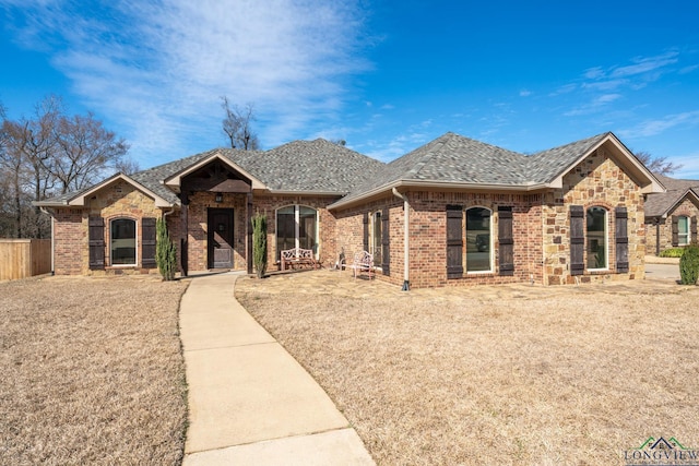 view of front of house featuring stone siding, a shingled roof, fence, and brick siding