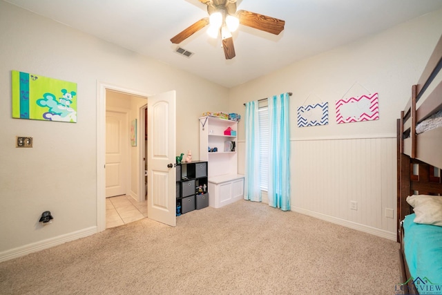 bedroom featuring light carpet, a wainscoted wall, visible vents, and a ceiling fan