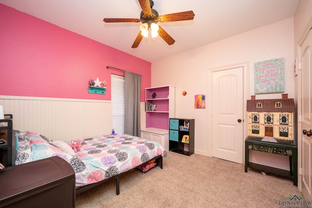 bedroom with light carpet, a ceiling fan, and wainscoting