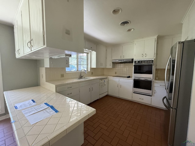 1705 Hyacinth Dr, Longview, TX 75601 - kitchen with black appliances, under cabinet range hood, tile counters, brick patterned floors, and decorative backsplash
