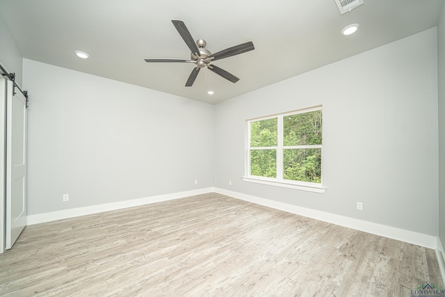 empty room featuring a barn door, ceiling fan, and light wood-type flooring