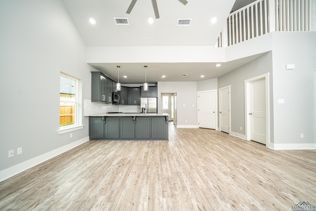 kitchen with a towering ceiling, stainless steel appliances, ceiling fan, pendant lighting, and gray cabinets