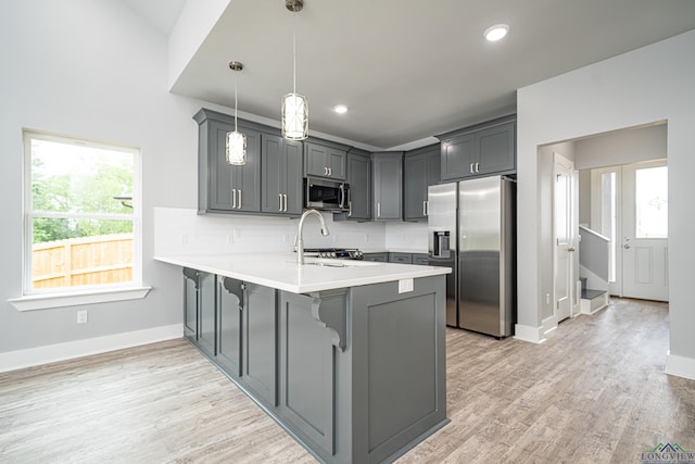 kitchen featuring backsplash, hanging light fixtures, gray cabinets, appliances with stainless steel finishes, and kitchen peninsula