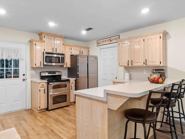 kitchen with a kitchen breakfast bar, light countertops, a peninsula, light brown cabinets, and stainless steel appliances