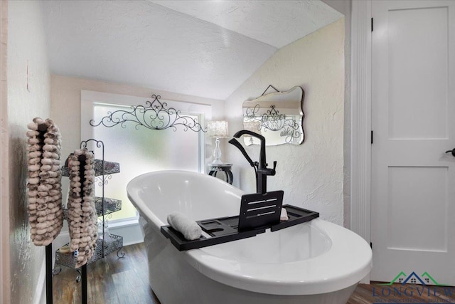 bathroom view of a textured wall, wood finished floors, a freestanding tub, and a textured ceiling
