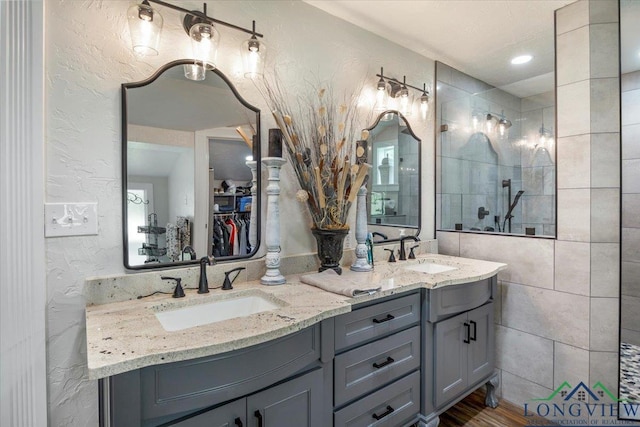 full bathroom featuring a textured wall, double vanity, walk in shower, and a walk in closet
