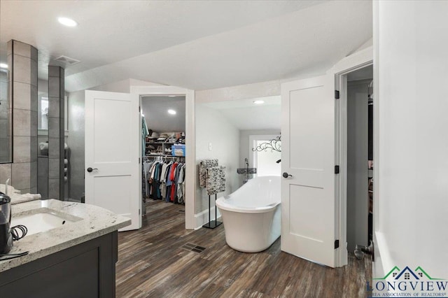 full bath featuring wood finished floors, a soaking tub, a spacious closet, vanity, and tiled shower