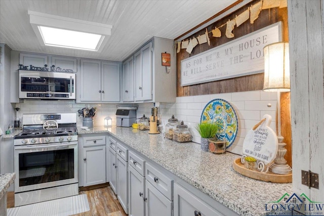 kitchen featuring appliances with stainless steel finishes, tasteful backsplash, light stone countertops, and light wood-style floors