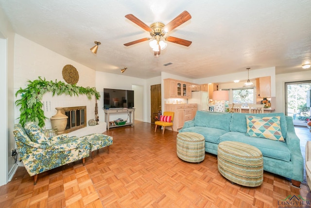 living room with ceiling fan, light parquet floors, a textured ceiling, and a brick fireplace