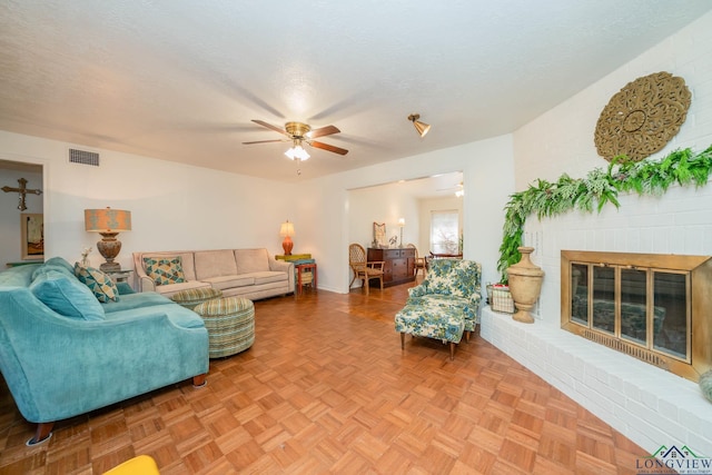 living room featuring ceiling fan, parquet floors, a textured ceiling, and a brick fireplace