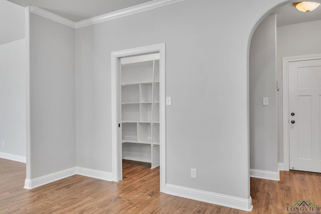interior space with arched walkways, ornamental molding, wood finished floors, and baseboards