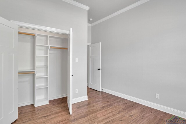 unfurnished bedroom with baseboards, ornamental molding, wood finished floors, and a closet
