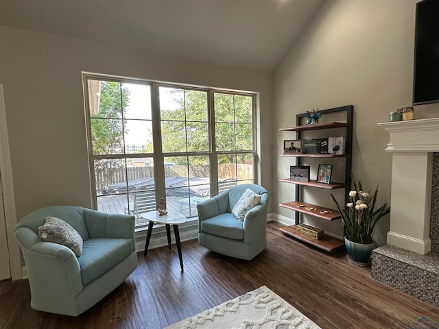 sitting room with vaulted ceiling, wood finished floors, a fireplace with raised hearth, and baseboards