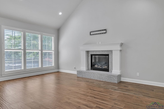 unfurnished living room with high vaulted ceiling, wood finished floors, a premium fireplace, baseboards, and recessed lighting