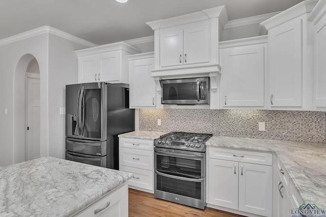 kitchen with white cabinets, crown molding, light stone countertops, and stainless steel appliances