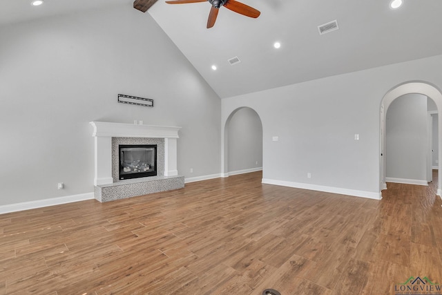 unfurnished living room with visible vents, arched walkways, ceiling fan, and high vaulted ceiling