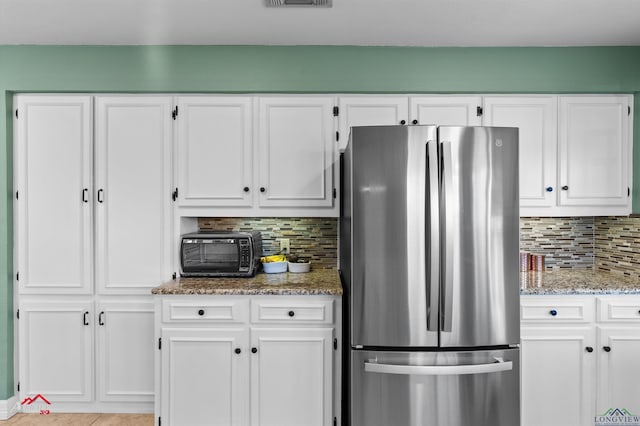 kitchen featuring light stone countertops, stainless steel fridge, backsplash, and white cabinetry