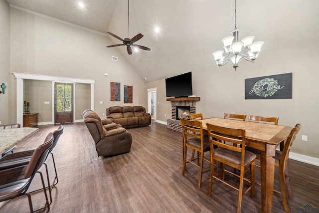 dining space with ceiling fan with notable chandelier, dark hardwood / wood-style flooring, high vaulted ceiling, and a brick fireplace