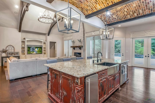 kitchen with hanging light fixtures, a stone fireplace, vaulted ceiling, brick ceiling, and a kitchen island with sink