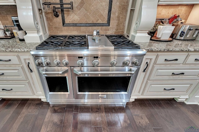 kitchen featuring light stone countertops, backsplash, range with two ovens, and dark wood-type flooring