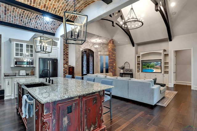 kitchen with refrigerator, brick ceiling, sink, a center island with sink, and white cabinets