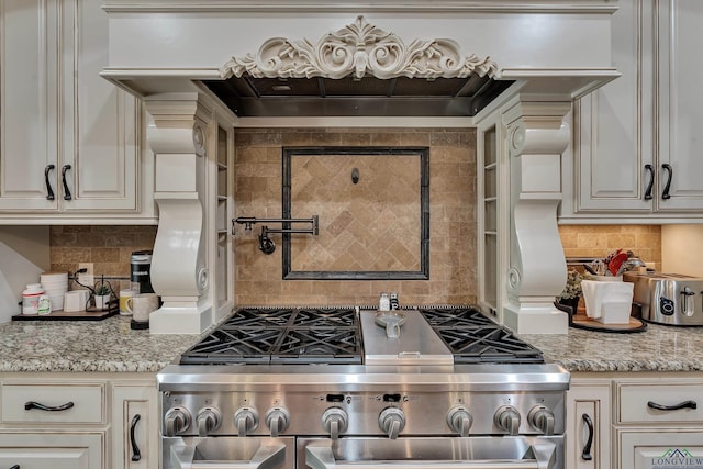 kitchen with decorative backsplash, light stone countertops, high end stainless steel range oven, and cream cabinets