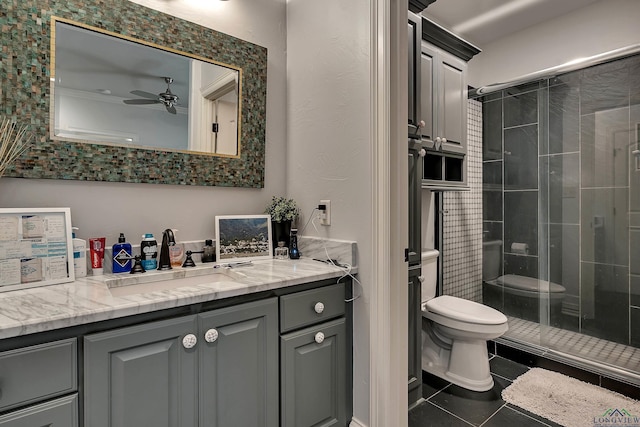 bathroom featuring vanity, a shower with door, ceiling fan, tile patterned flooring, and toilet