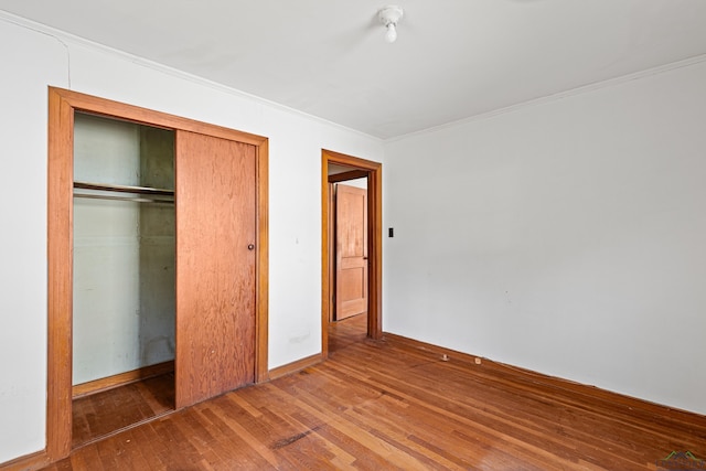 unfurnished bedroom featuring wood-type flooring, ornamental molding, and a closet