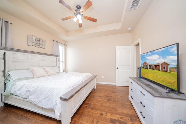 bedroom with dark hardwood / wood-style flooring, a raised ceiling, and ceiling fan