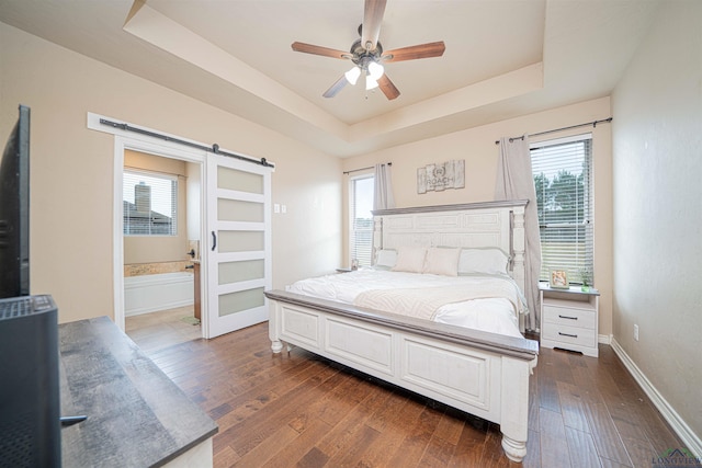 bedroom featuring dark hardwood / wood-style flooring, a tray ceiling, ceiling fan, a barn door, and multiple windows