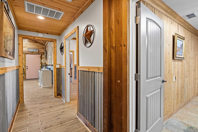 hallway with crown molding, wooden walls, light hardwood / wood-style flooring, and wood ceiling