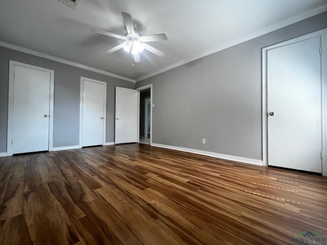 unfurnished bedroom with ceiling fan, dark hardwood / wood-style floors, crown molding, and two closets