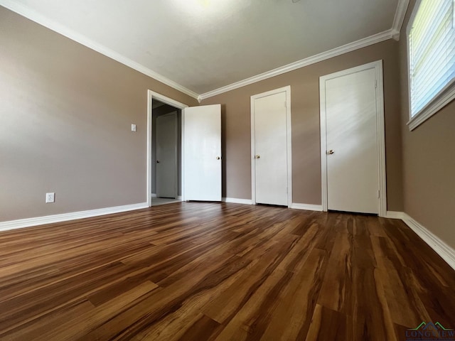 unfurnished bedroom with dark hardwood / wood-style flooring, two closets, and ornamental molding