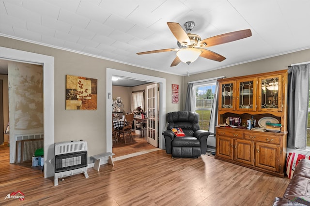 living area with crown molding, a ceiling fan, heating unit, and light wood finished floors
