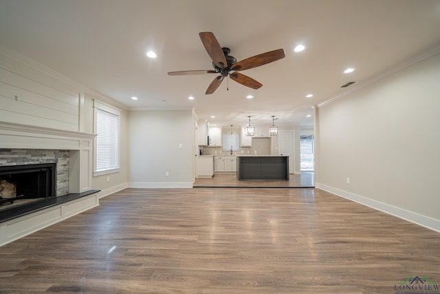 unfurnished living room featuring a stone fireplace, ceiling fan, dark hardwood / wood-style floors, and ornamental molding