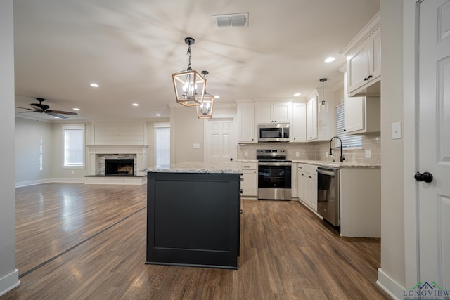 kitchen with white cabinetry, a center island, hanging light fixtures, stainless steel appliances, and ceiling fan with notable chandelier