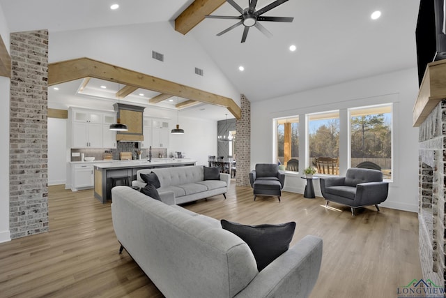 living room featuring sink, high vaulted ceiling, light wood-type flooring, beamed ceiling, and ceiling fan with notable chandelier