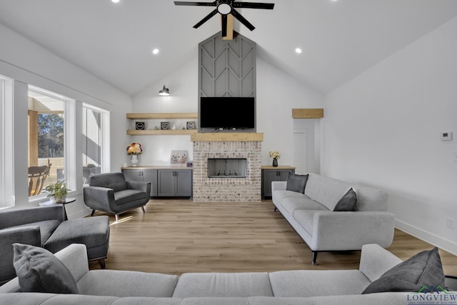 living room featuring ceiling fan, a fireplace, high vaulted ceiling, and light hardwood / wood-style flooring