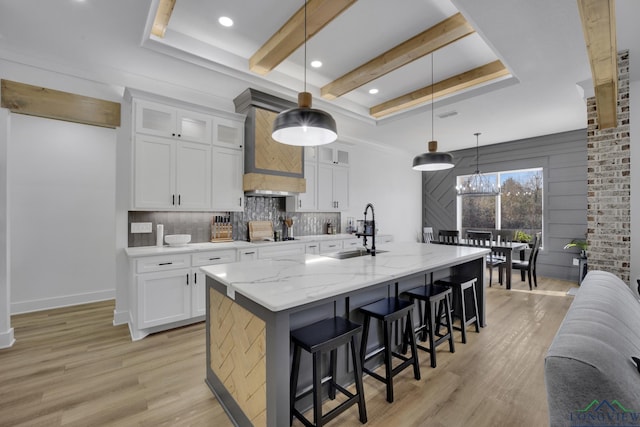 kitchen featuring hanging light fixtures, white cabinetry, sink, and a center island with sink