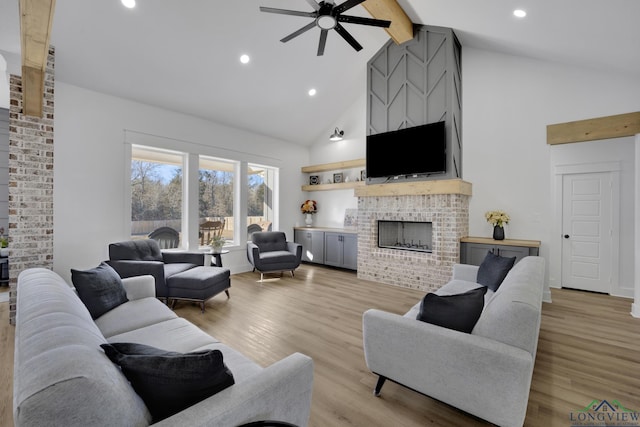 living room featuring high vaulted ceiling, beamed ceiling, ceiling fan, a fireplace, and light hardwood / wood-style floors