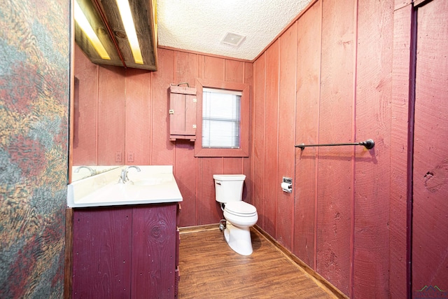 bathroom featuring a textured ceiling, vanity, hardwood / wood-style flooring, toilet, and wood walls