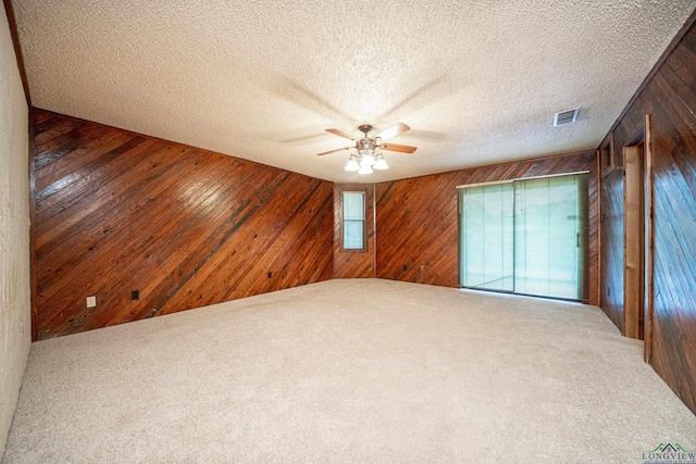 unfurnished room featuring carpet flooring, a textured ceiling, ceiling fan, and wooden walls