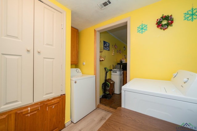 clothes washing area featuring light wood-type flooring, visible vents, cabinet space, and washer and clothes dryer