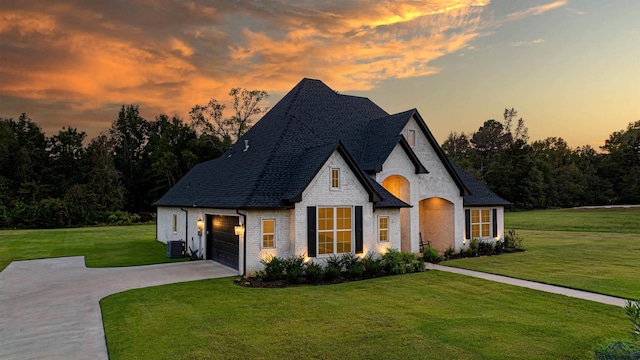 french country inspired facade with a lawn, central AC unit, and a garage