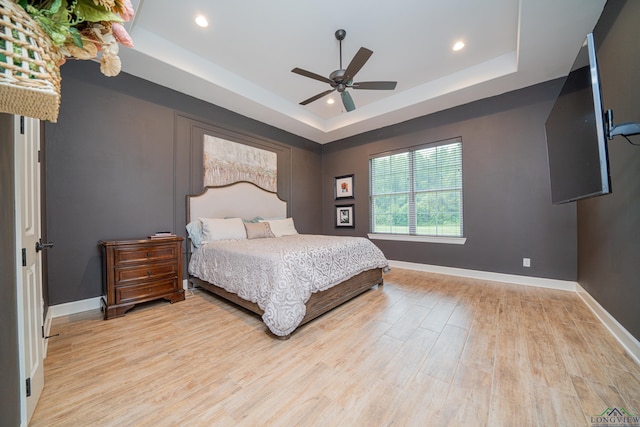 bedroom with light hardwood / wood-style flooring, a raised ceiling, and ceiling fan