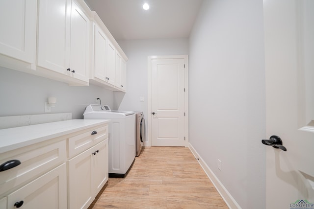 laundry room with washer and dryer, light wood-type flooring, and cabinets