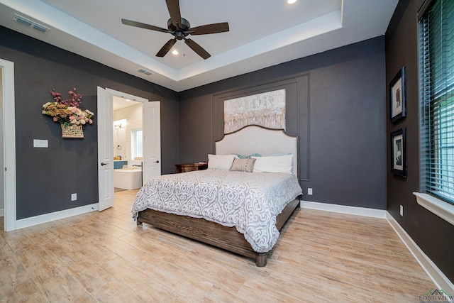 bedroom with a raised ceiling, ceiling fan, light hardwood / wood-style flooring, and ensuite bathroom