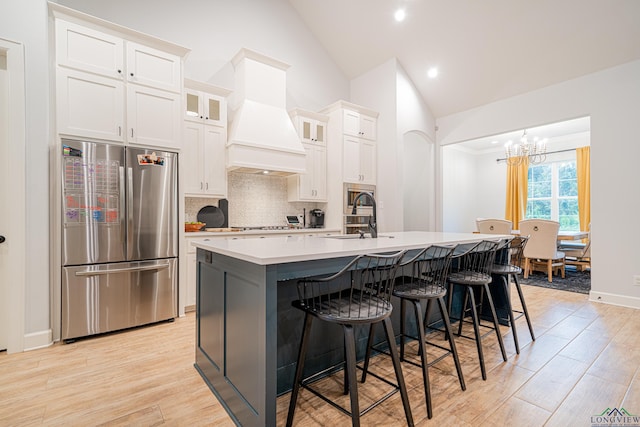 kitchen with lofted ceiling, premium range hood, a kitchen island with sink, sink, and appliances with stainless steel finishes