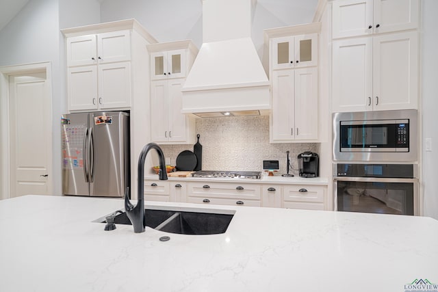 kitchen with sink, light stone counters, backsplash, appliances with stainless steel finishes, and custom exhaust hood